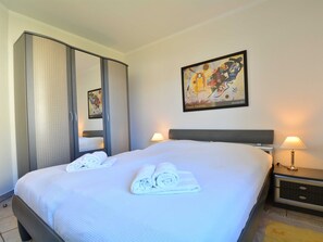 Ett hotellrum med en stor säng, två sänglampor, en tavla på väggen och en garderob med en spegel.
