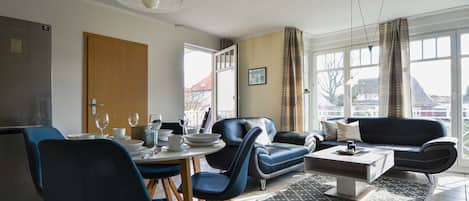 A modern living room with a dining area, featuring a sofa, chairs, a coffee table, and a dining table set for four.