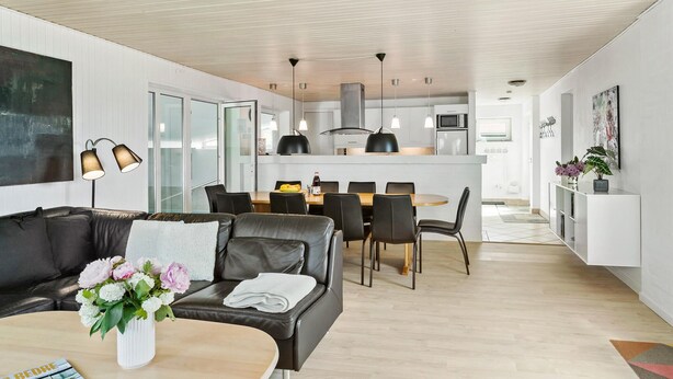 A modern living room with a leather sofa, a dining table with chairs, and a kitchen area with a microwave and stove. - Awesome home in Væggerløse with sauna (Væggerløse)