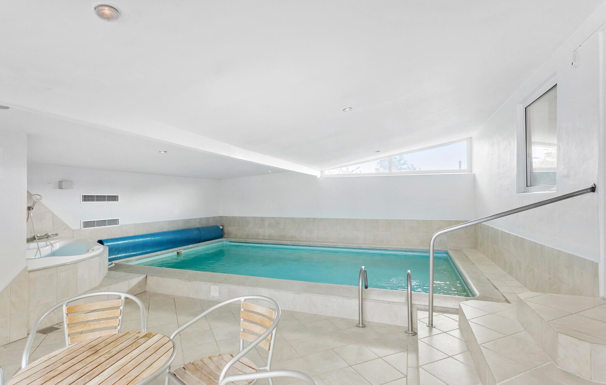 Une piscine intérieure moderne avec une vue dégagée sur le plafond, un jacuzzi et un espace détente avec des fauteuils.