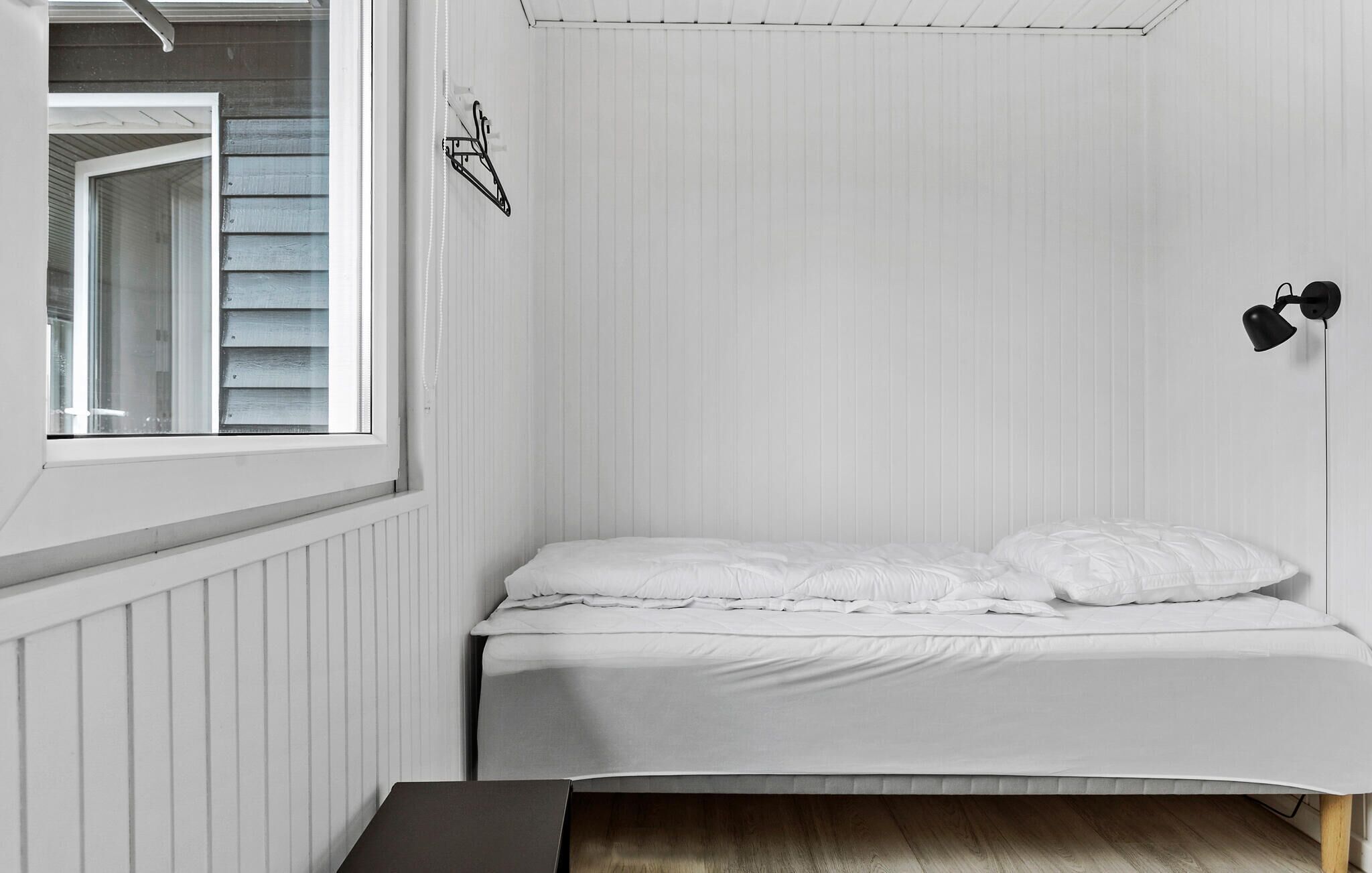 Una camera da letto con un letto singolo, una finestra e una lampada fissata al muro.