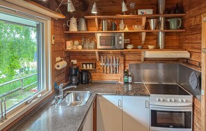 Een keuken met houten wanden, een roestvrijstalen spoelbak, een magnetron, een fornuis en diverse keukengerei en apparaten.