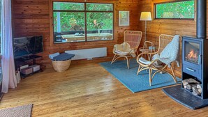 Un intérieur de chalet chaleureux avec une cheminée, des fauteuils en osier, un téléviseur et de grandes fenêtres.