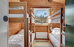 Eine kleine Holzhütte mit Etagenbetten, einem Fenster mit Blick auf Bäume und einer Tür.