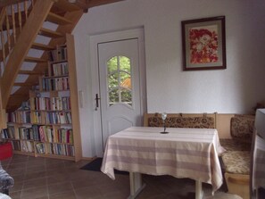 A room with a staircase, a bookshelf, a table with a tablecloth, a sofa, and a door with a window.