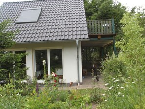 A house with a tiled roof, a balcony with a railing, and a garden with various plants and flowers.