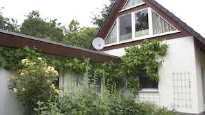 A house with a sloped roof, a satellite dish, and a garden with roses. - Flower House - Flower House * (Rankwitz)