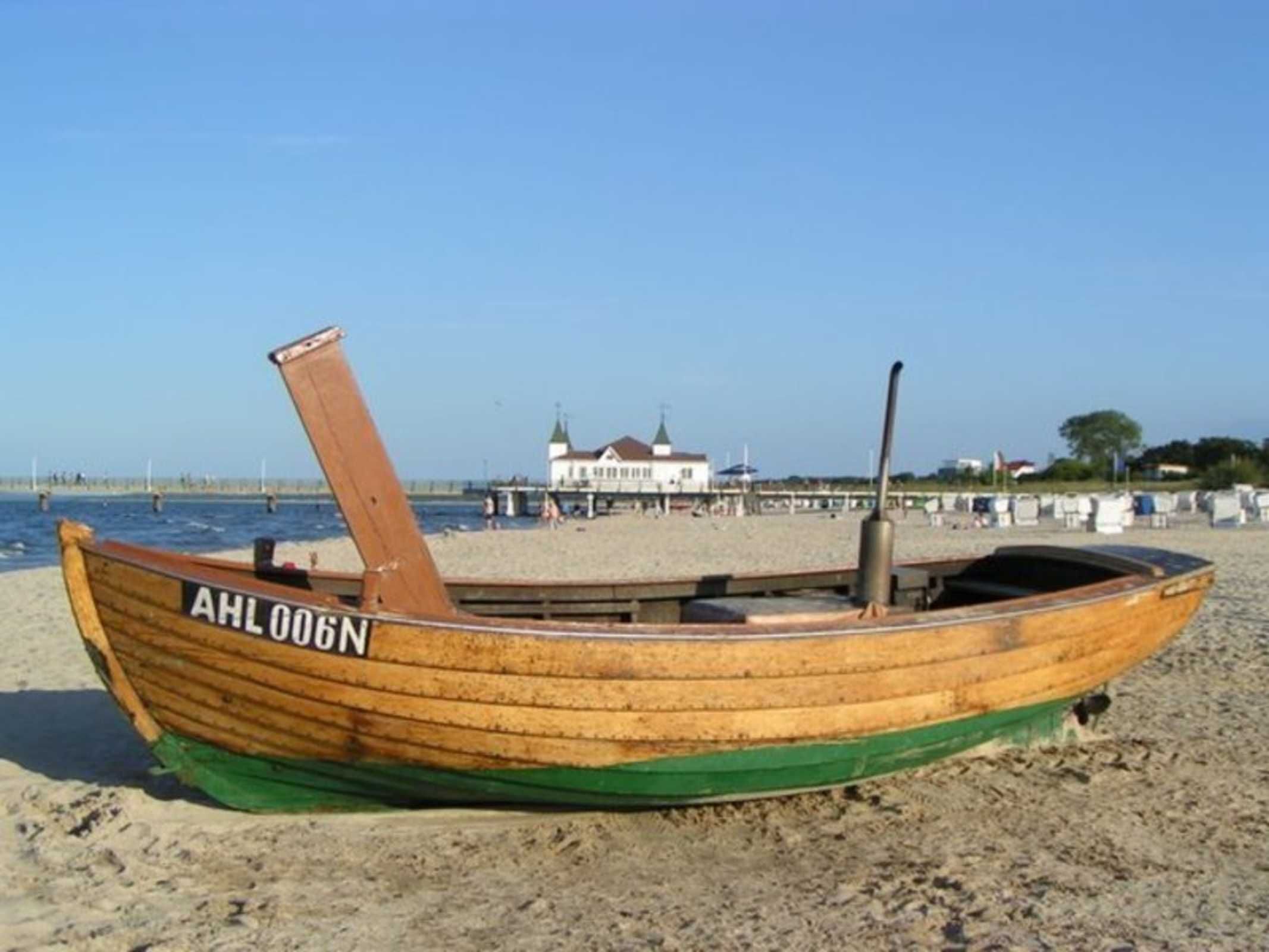 Una lancha de madera con el número de identificación AHL 006N en una playa arenosa.