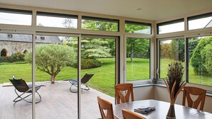 A dining area with a table and chairs, large windows, and a view of a garden and stone building. - 3 bedroom gorgeous home in Lamballe-Armor (Lamballe-Armor)
