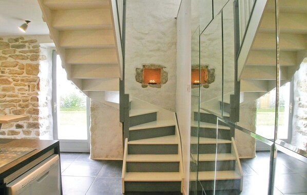 Ein modernes Interieur mit Steinwand, einer Treppe mit Glasgeländern und zwei beleuchteten Wandleuchten.
