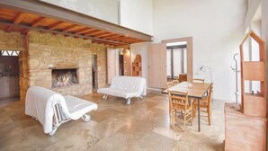 A spacious living area with a stone fireplace, a dining table with chairs, and a cozy seating area with covered chairs.