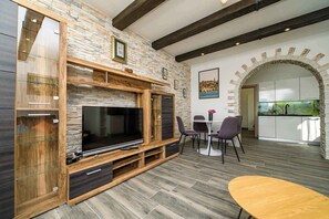 A modern living room with a stone wall, wooden entertainment unit, and a dining area with a round table and chairs.