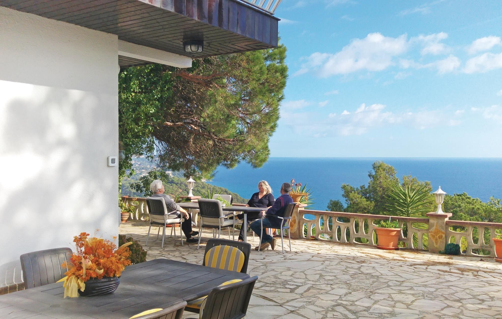 An outdoor seating area with stone flooring, tables, and chairs, overlooking a scenic view of the sea.