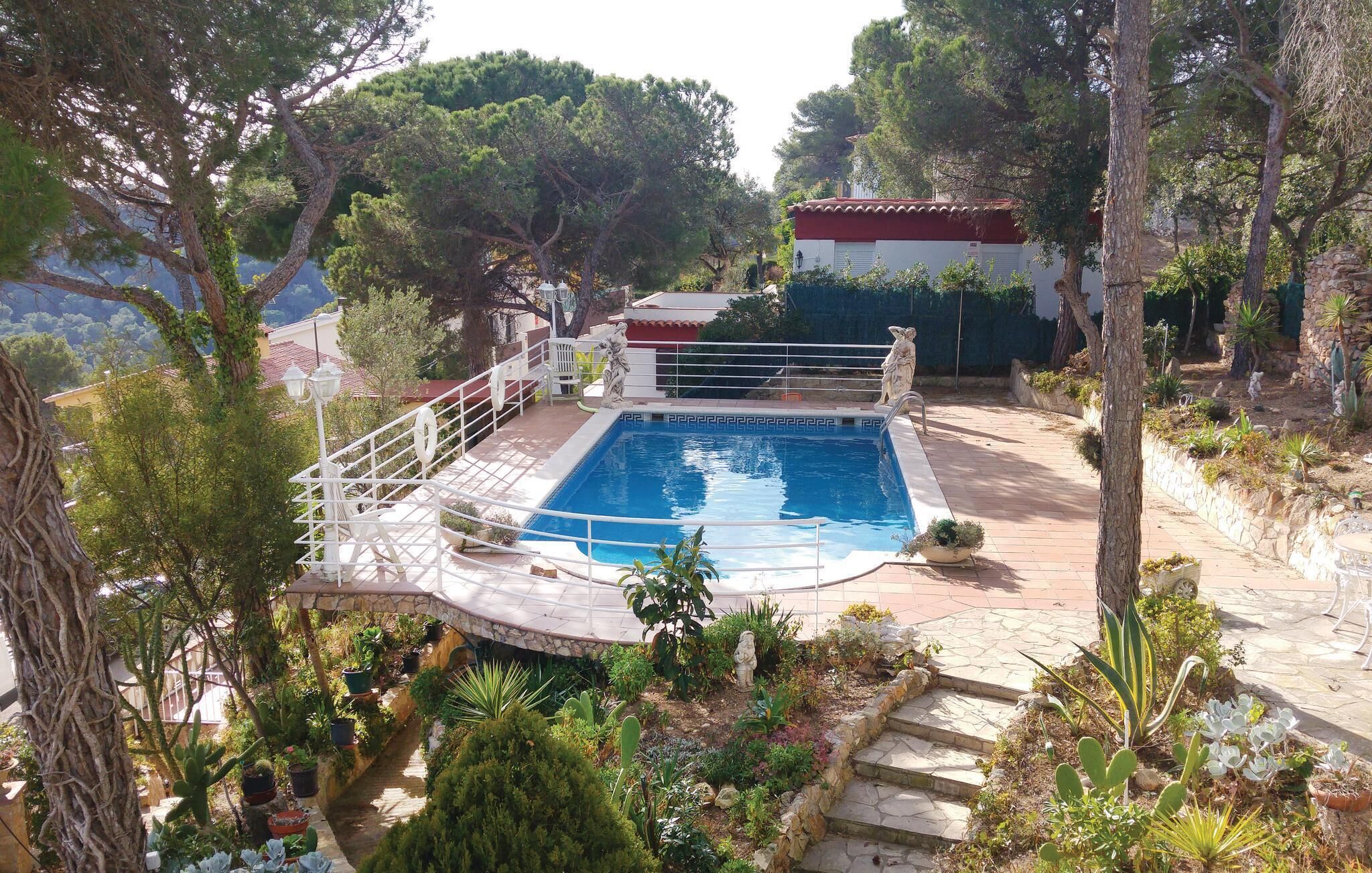 En swimmingpool omgiven av en stenbelagd terrass, med en staty och en liten byggnad i bakgrunden.