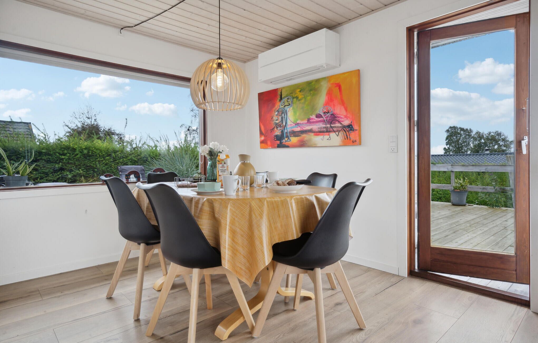 Un espace repas avec une table ronde, des chaises noires, un plafond en bois et une grande fenêtre donnant sur un paysage verdoyant.