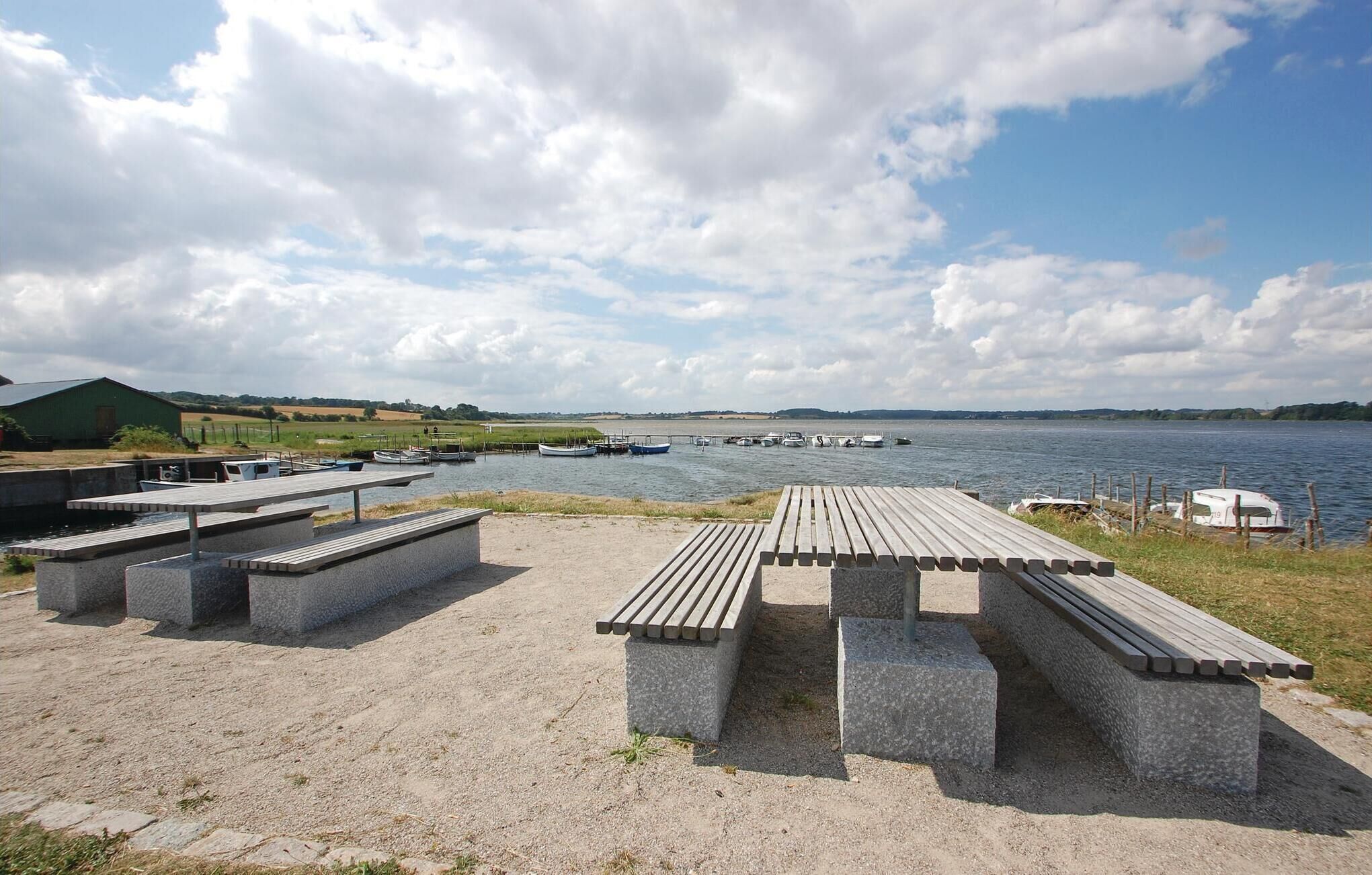 Un espace de pique-nique au bord du lac, avec des bancs en béton et un quai où sont amarrés des bateaux.