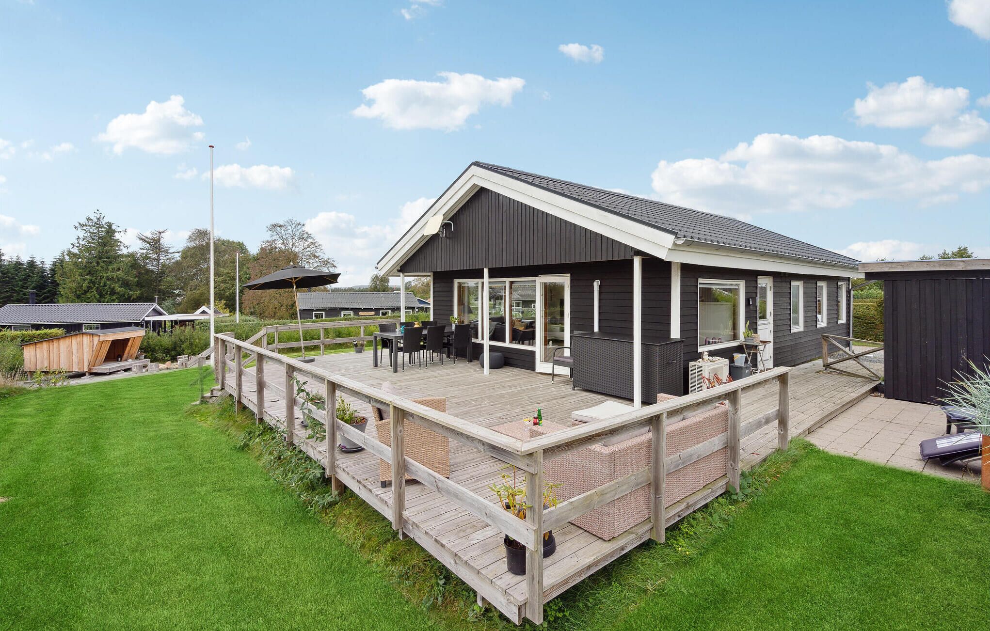 Ein modernes Haus mit einer Terrasse, einer Veranda und einem großen Fenster mit Blick auf einen Garten.