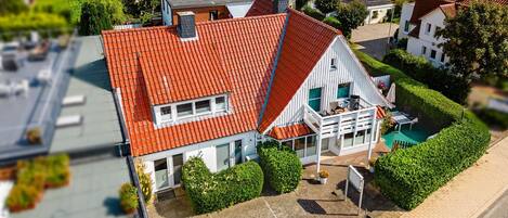 Une maison avec un toit recouvert de tuiles rouges, un balcon et un jardin.