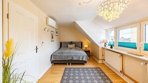 Quarto com cama, radiador, janela com persianas, candelabro e porta.