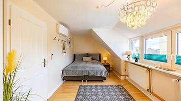 A bedroom with a bed, a radiator, a window with blinds, a chandelier, and a door.