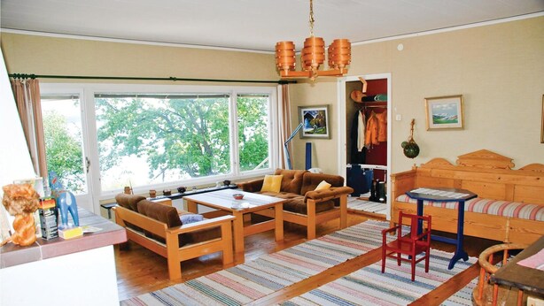 A cozy living room with a sofa, two armchairs, a coffee table, and a small table with chairs. There is a window with curtains, a door, and a hanging light fixture. - Awesome home in Värnamo with kitchen (Värnamo)