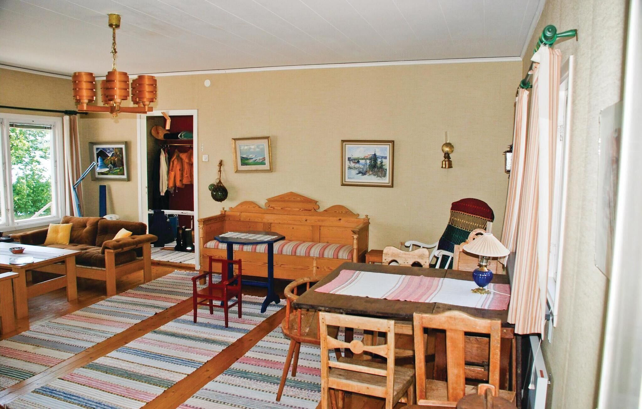 Un saló acollidor amb un sofà de fusta, una taula petita i una cadira. Hi ha un armari amb roba penjada a l'interior, i una finestra amb cortines.