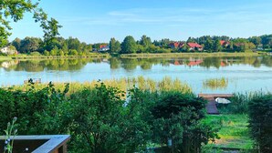 Un lago con un muelle, rodeado de vegetación y casas al fondo.