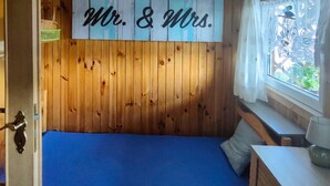 Un dormitorio con cabecera de madera, una cama con colchón azul, una mesita de noche pequeña y una ventana con vistas a la vegetación.