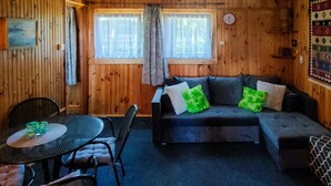 Un interior de madera con un sofá, dos sillones, una mesa con vasos y un reloj en la pared.