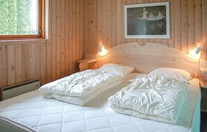 A bedroom with a wooden paneled wall, a bed with white bedding, a nightstand, a bedside table, and a framed picture above the bed. - Nice home in Hejls with WiFi (Hejls)