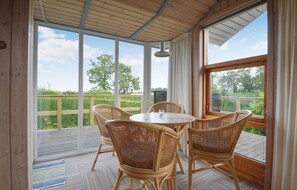 A covered patio with a round table and four wicker chairs, large windows offering a view of greenery, and a wooden ceiling. - Nice home in Hejls with WiFi (Hejls)
