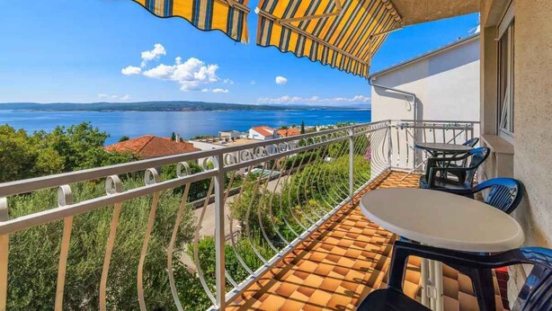 Een balkon met uitzicht op zee, een tafel en stoelen.