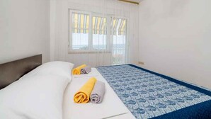 Een hotelkamer met een bed, twee opgerolde handdoeken, een raam met gordijnen en een bed met een decoratief sprei.