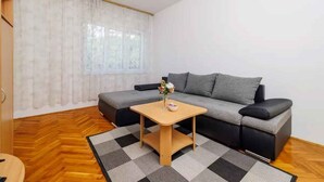 Een woonkamer met een grijze bank, een houten salontafel en een kamerkleed met dessin.