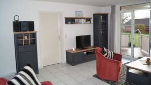 A living room with a TV, bookshelf, and a red sofa. - Ressing Vacation Rental - - Ressing Vacation Rental (Brodersby)
