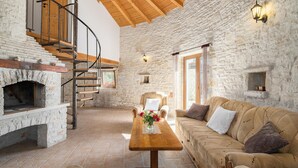 Un intérieur rustique avec une cheminée en pierre, un escalier en bois, un canapé et une table à manger.