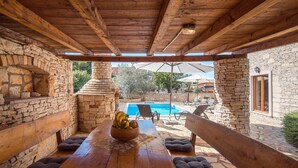 Une pergola en bois avec un mur en pierre, une cheminée en pierre, une piscine et un espace salon extérieur.