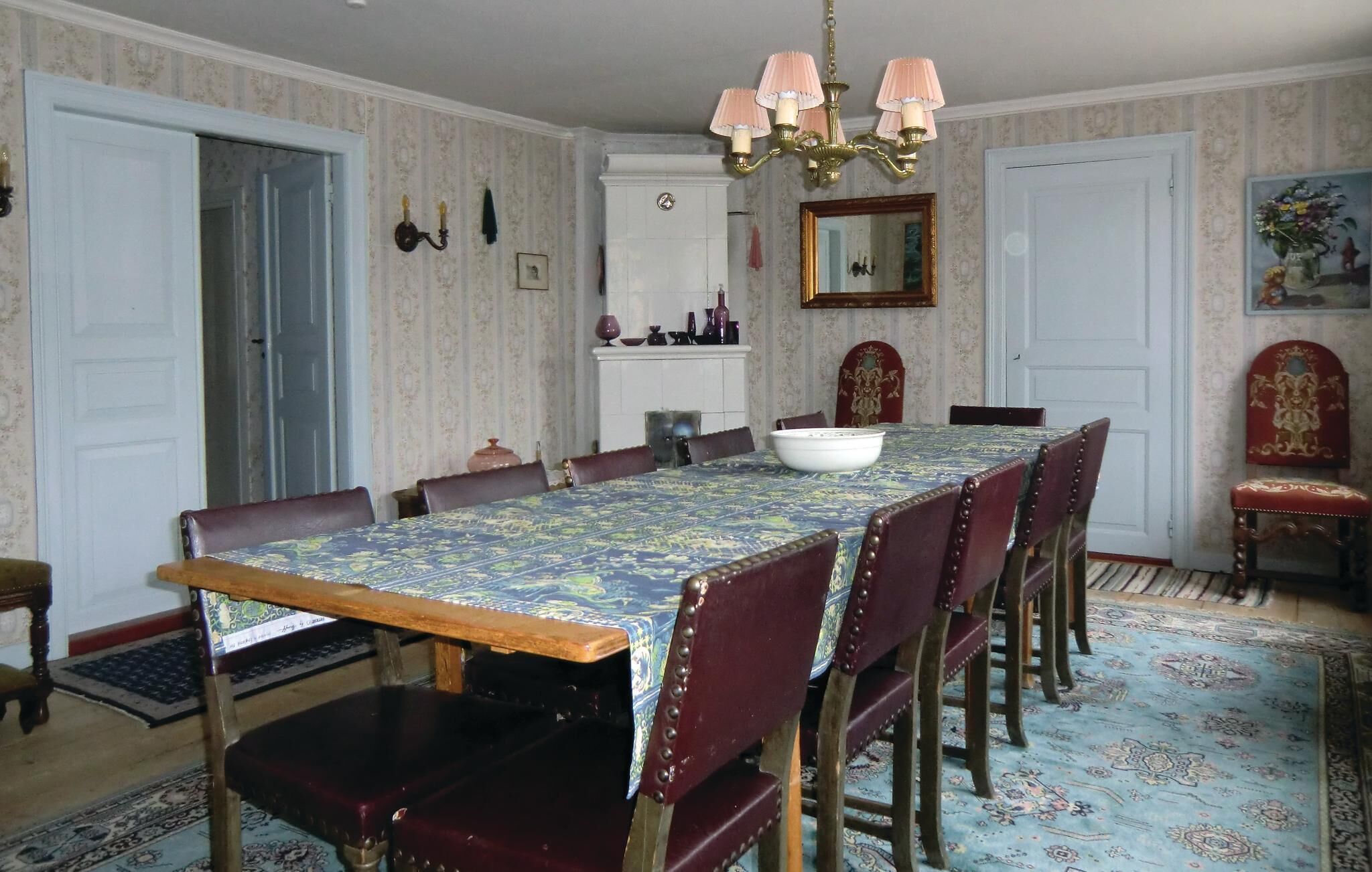 Un comedor con una mesa larga, sillas, una araña y papel tapiz estampado.
