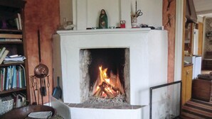 A fireplace with a fire burning inside, surrounded by a bookshelf and various items on the mantel.