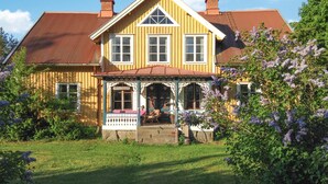 A two-story house with a porch, a small garden, and a red roof.