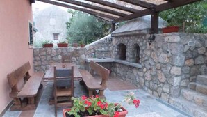 Un patio exterior con paredes de piedra, bancos de madera, una mesa y una jardinera con flores.