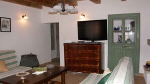 Una sala de estar con un sofá, una mesa de centro, un televisor sobre un mueble de madera y un aparador con puertas de cristal.
