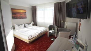 Ein Hotelzimmer mit Bett, Schreibtisch, Stuhl, Fernseher und einem Fenster mit Vorhängen.