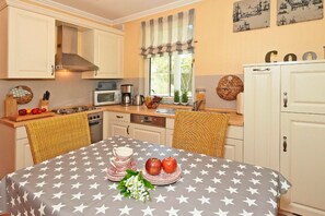Cozinha com armários brancos, micro-ondas, fogão e mesa de jantar com toalha de mesa estampada.