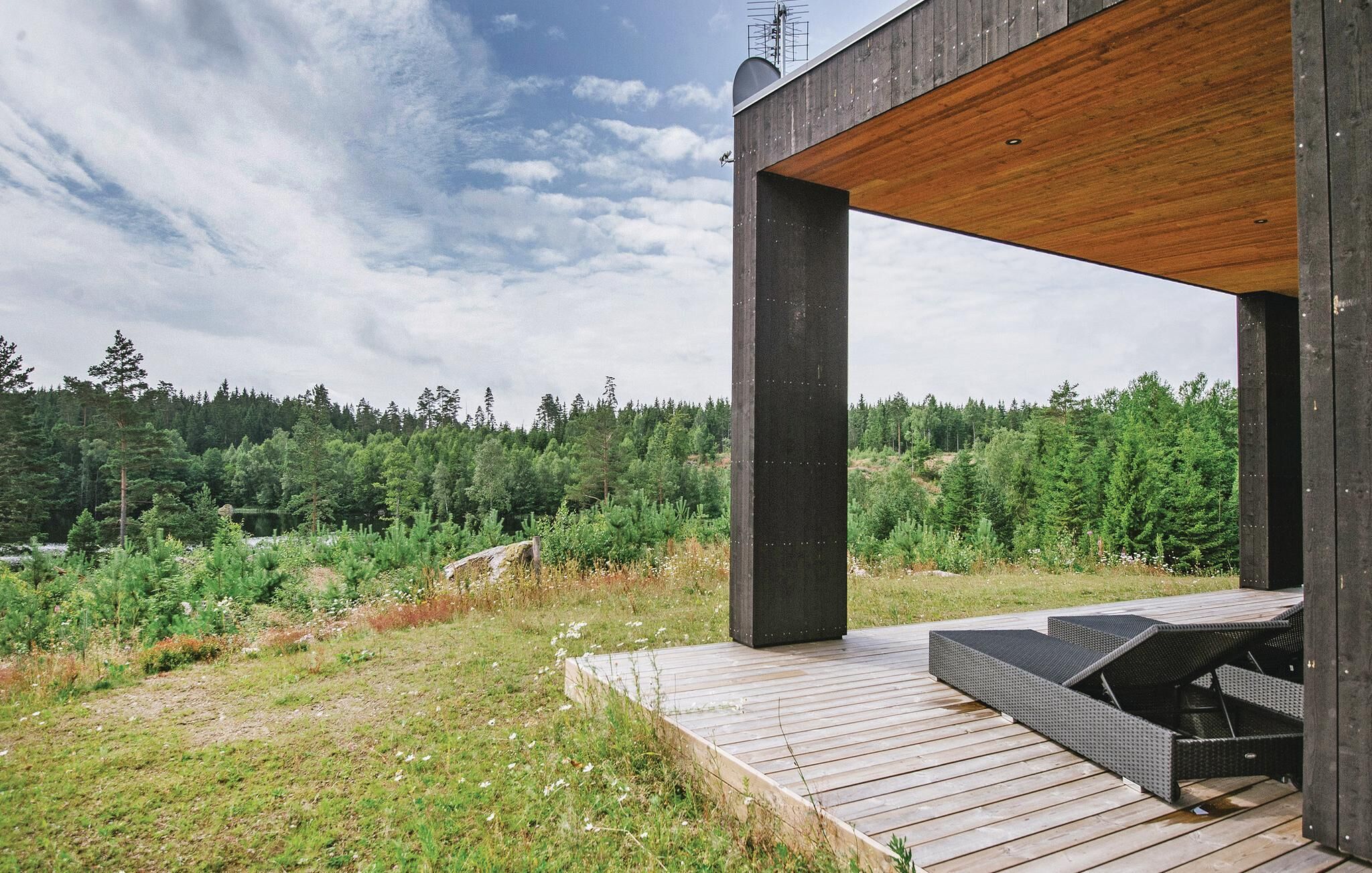 Una terraza moderna al aire libre con techo de madera y pilares metálicos, con vistas a un paisaje boscoso.