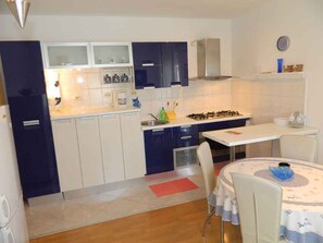 Une cuisine compacte avec des meubles blancs et bleu foncé, une cuisinière à gaz et un coin repas comprenant une table et des chaises.