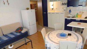 A compact living space with a sofa, a dining table with chairs, a refrigerator, and a kitchen area with cabinets and a sink. - Holiday apartment with internet access (Valbandon)