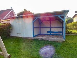 Een klein, laag bij de grond liggend tuinhuisje met schuin dak en een overdekte veranda.