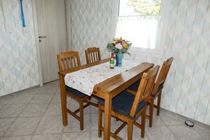 Een eettafel met een tafelkleed met bloemenmotief, houten stoelen, een vaas met bloemen en een fles champagne.