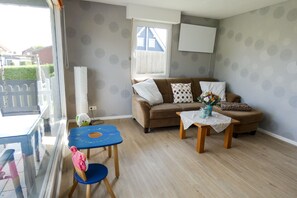 Een gemeubileerde woonkamer met een bank, een klein tafeltje, een blauwe stoel en een raam met uitzicht op een huis.